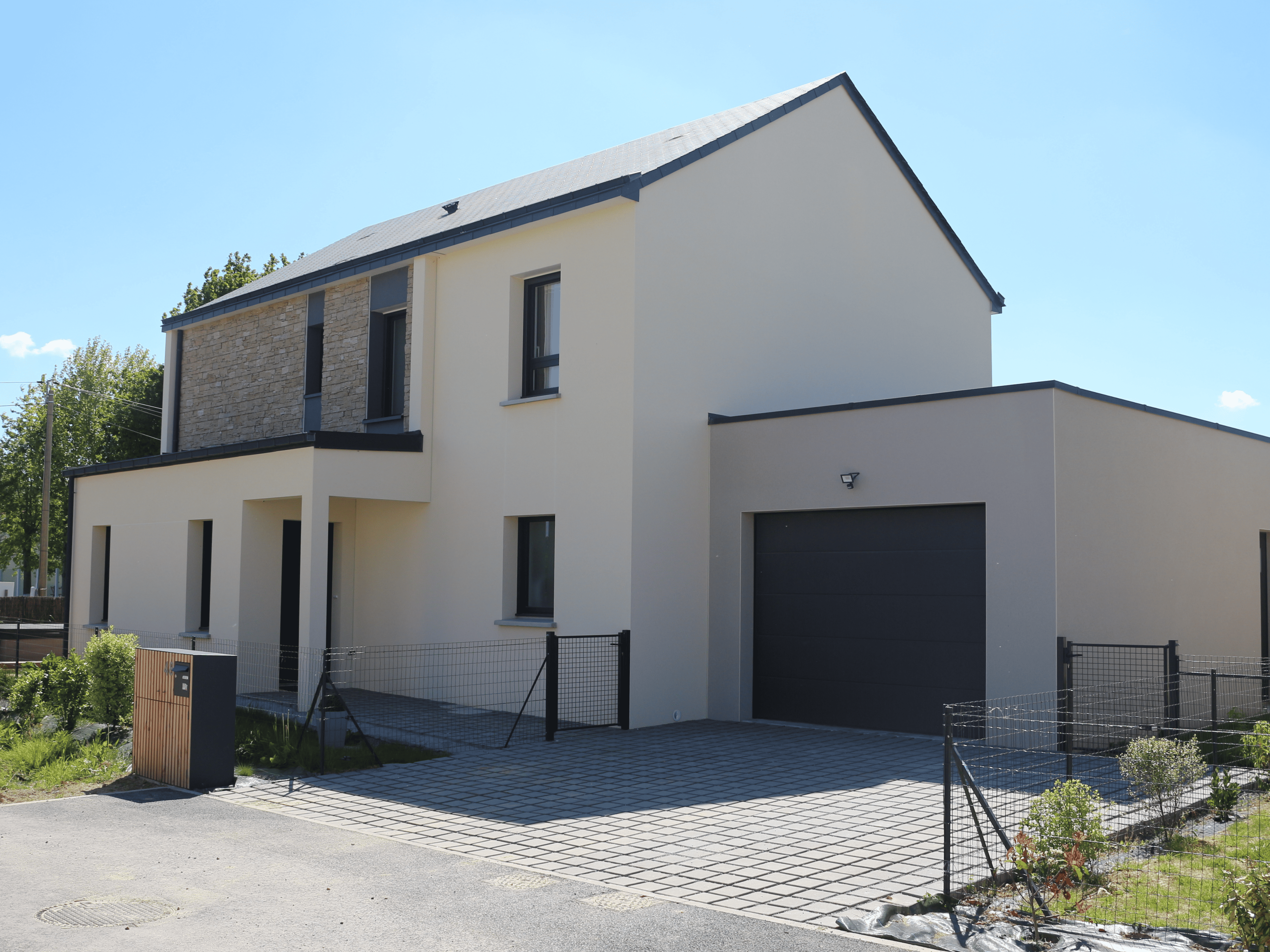 Maison contemporaine à toit plat et à double pente avec garage intégré et façade en enduit clair et parement en pierres Maison contemporaine à toit plat et à double pente avec garage intégré et façade en enduit clair et parement en pierres