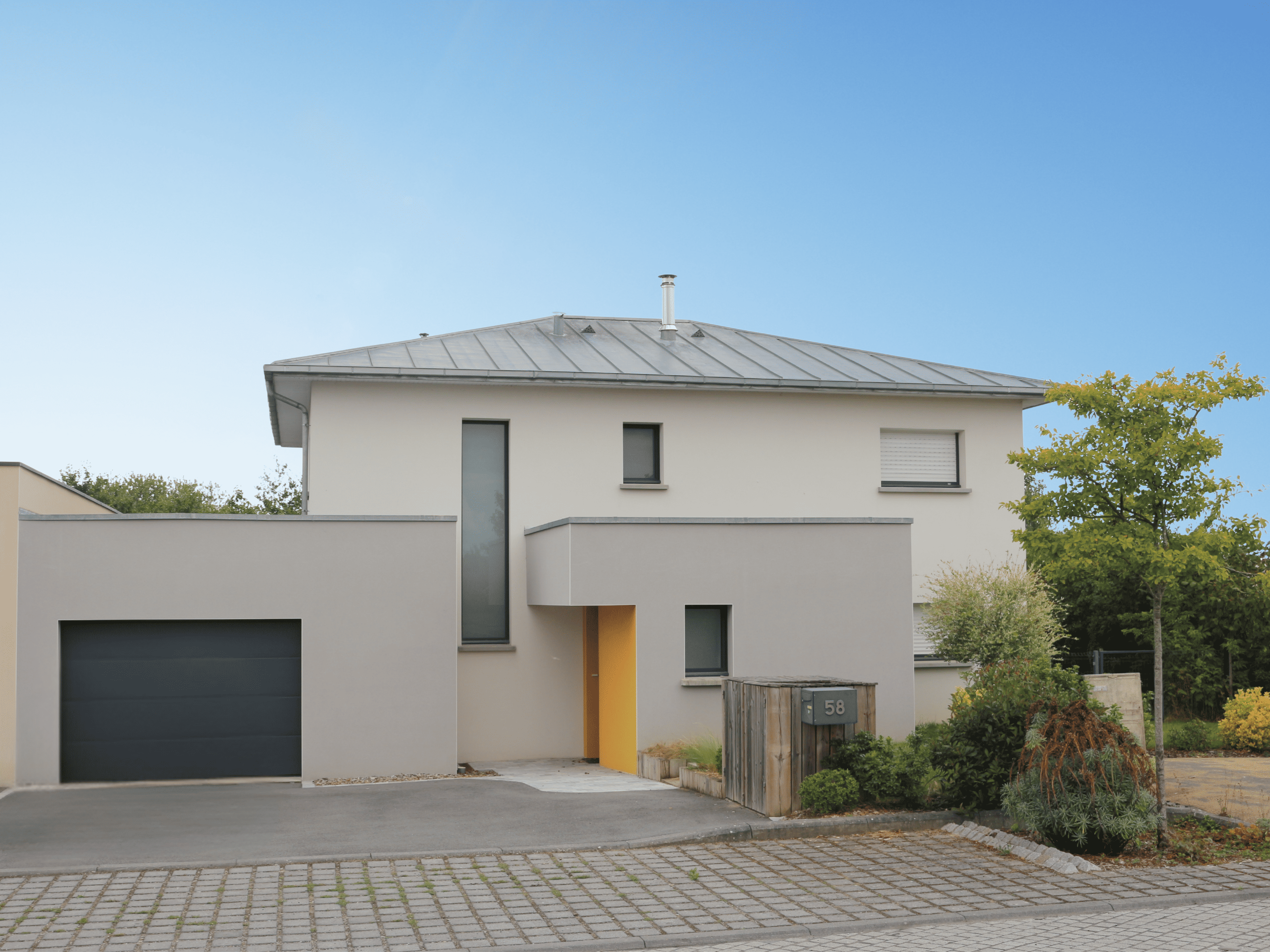 Maison contemporaine à étage avec toiture en zinc à 4 pans, façade enduite, baie verticale, garage accolé et jardin paysager. Maison contemporaine à étage avec toiture en zinc à 4 pans, façade enduite, baie verticale, garage accolé et jardin paysager.