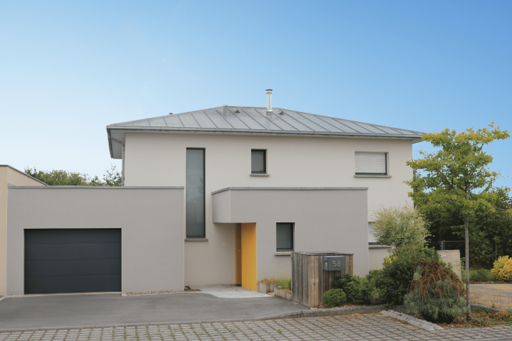 Maison contemporaine à étage avec toiture en zinc à 4 pans, façade enduite, baie verticale, garage accolé et jardin paysager.